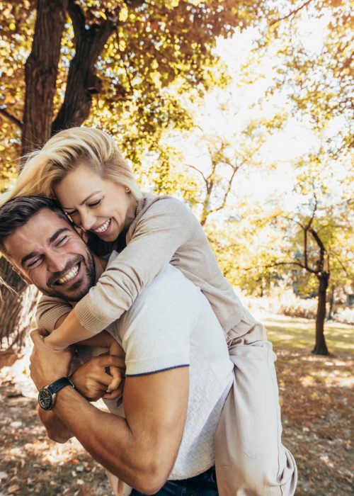 Boyfriend carrying his girlfriend on piggyback in autumn park.